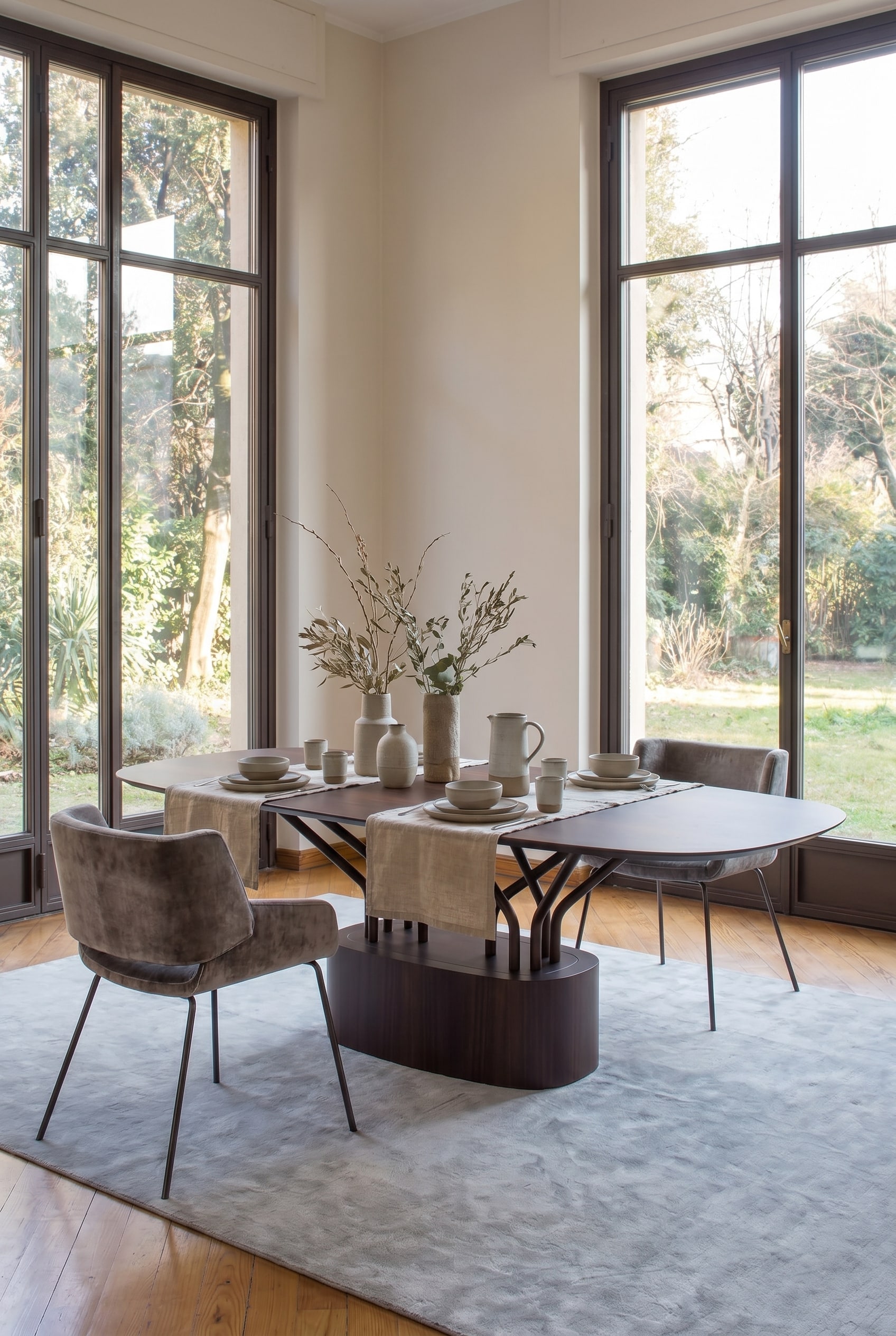 Modern dining room with a striking wooden table whose legs form an open lattice structure, accompanied by gray upholstered chairs