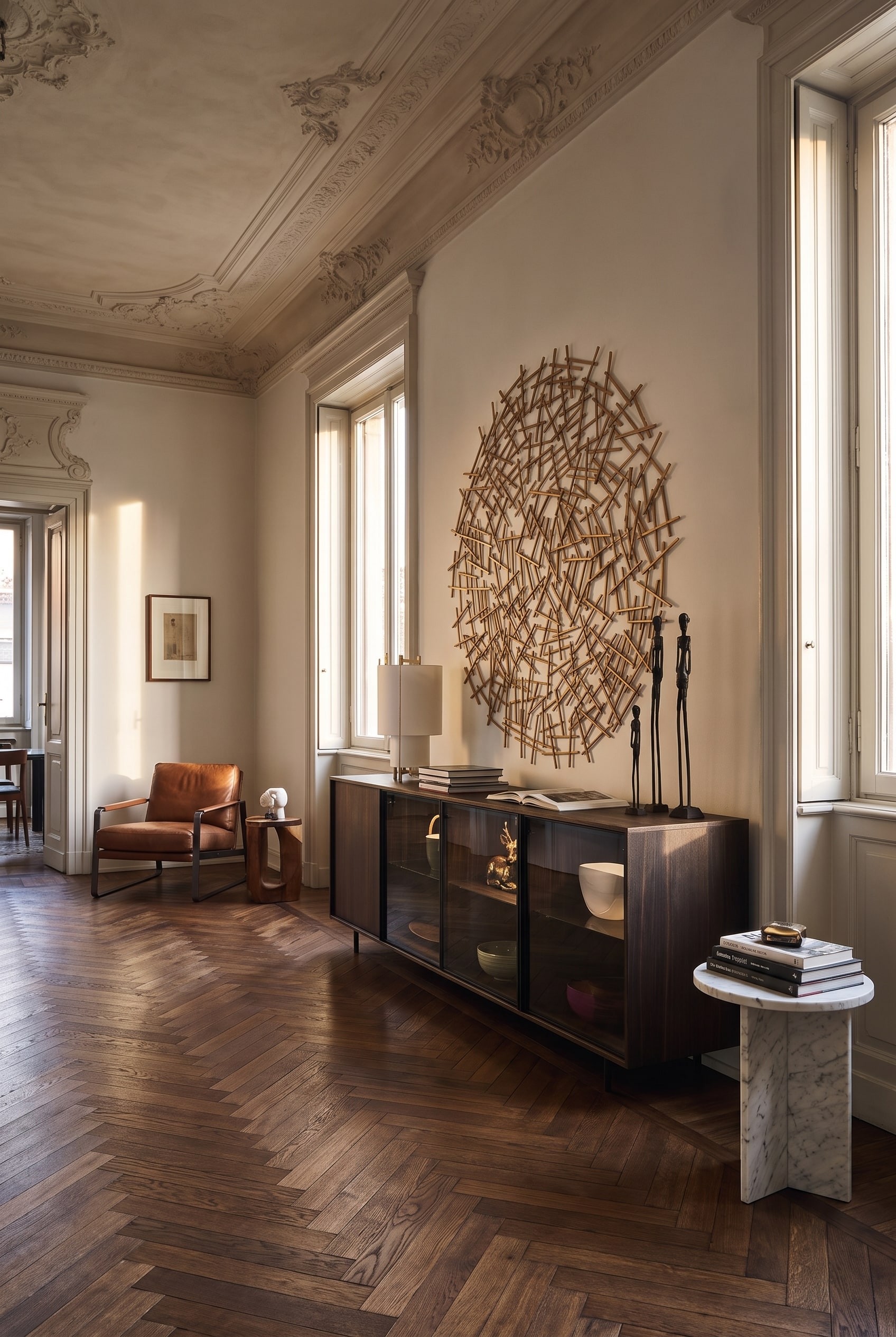 Ein langgestrecktes Glas-Sideboard auf schwarzen Metallkufen an einer Wand in einem Altbauzimmer, unter dem das Eichen-Fischgr&auml;tparkett ununterbrochen weiterl&auml;uft.