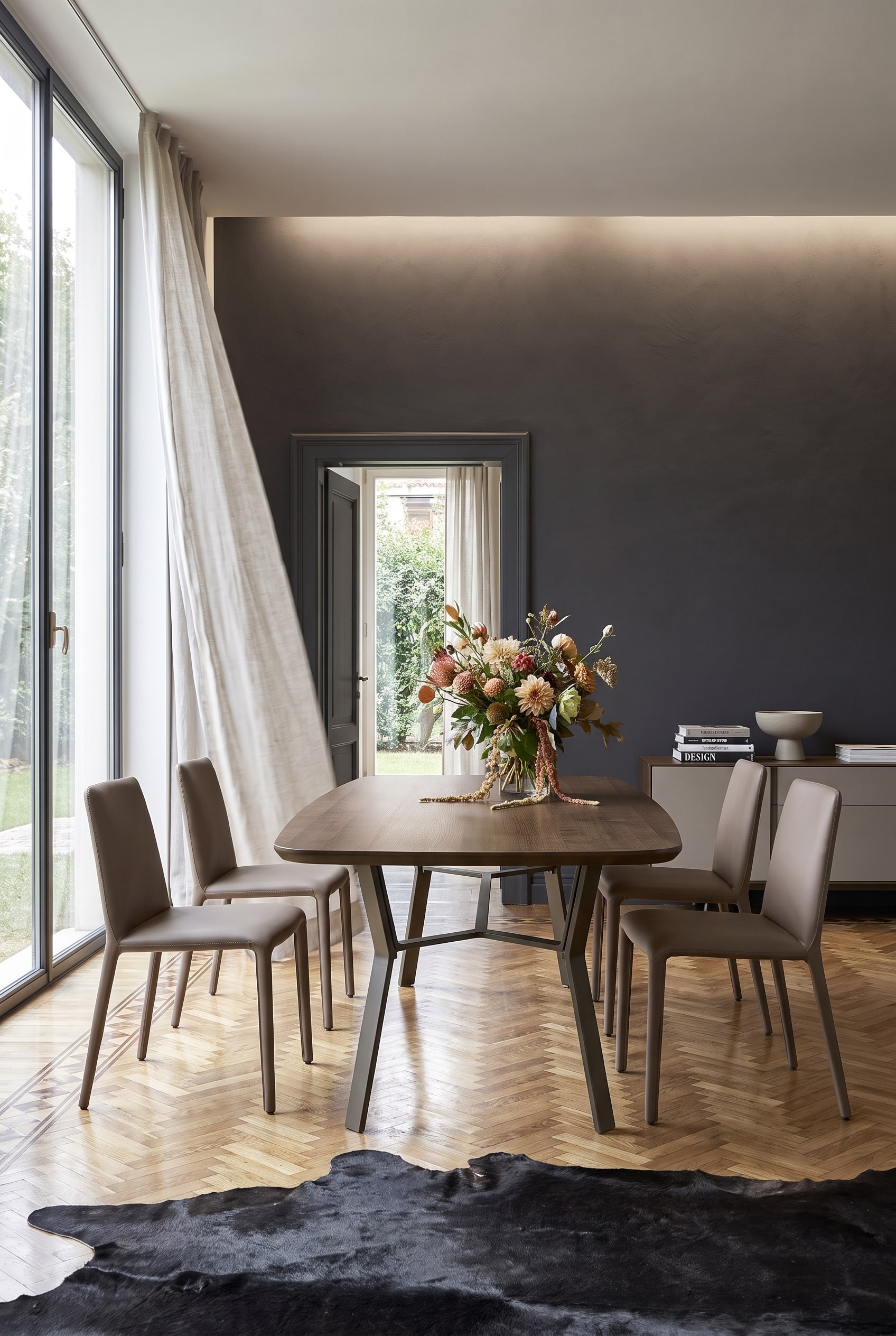 Minimalistisches Esszimmer mit dunkler Akzentwand, Holztisch auf Eisengestell und vier taupefarbenen Lederst&uuml;hlen