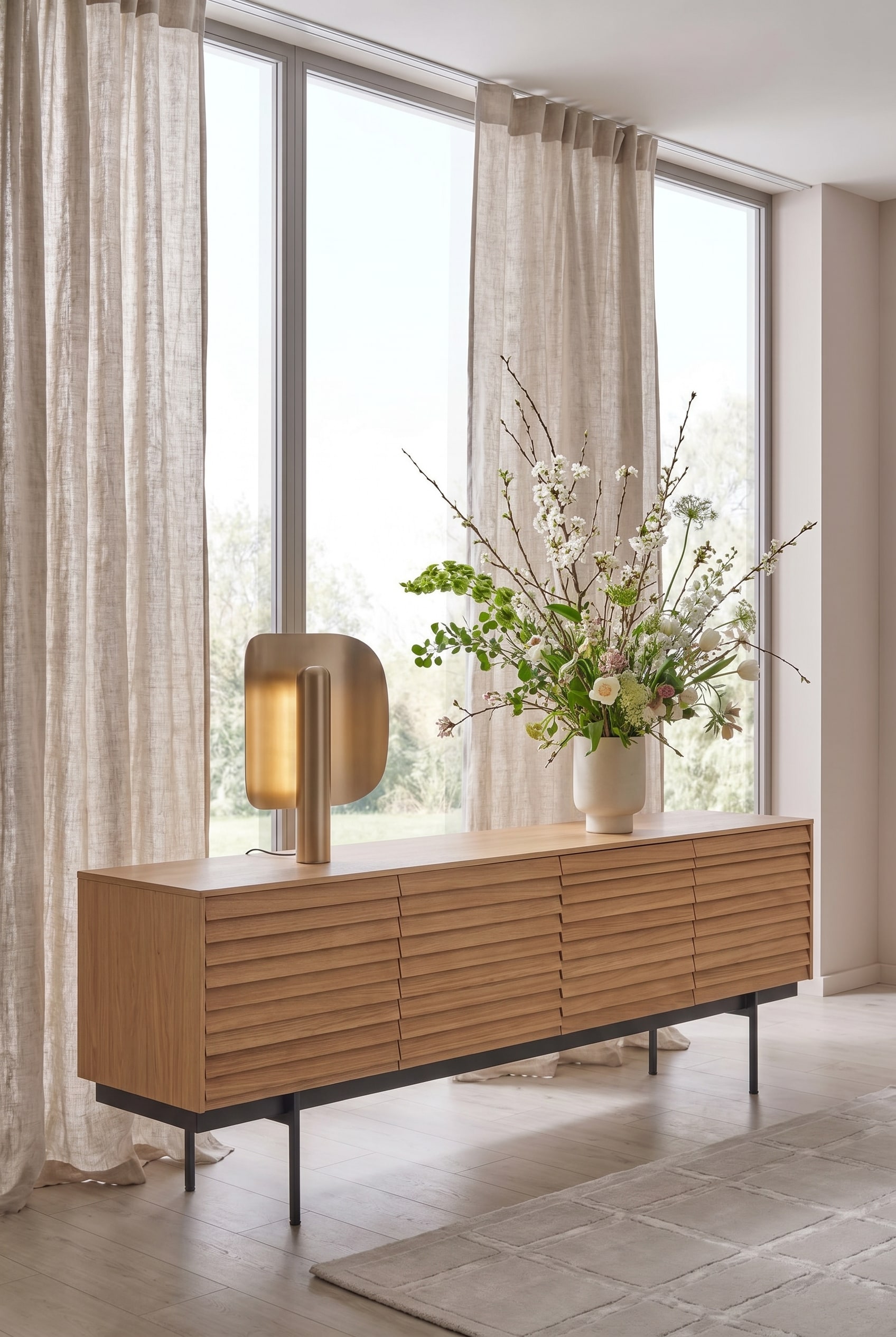 Minimalistisches Wohnzimmer mit einem Sideboard mit Holzlamellen, darauf ein großes asymmetrisches Frühlingsbouquet Minimalistisches Wohnzimmer mit einem Sideboard mit Holzlamellen, darauf ein großes asymmetrisches Frühlingsbouquet