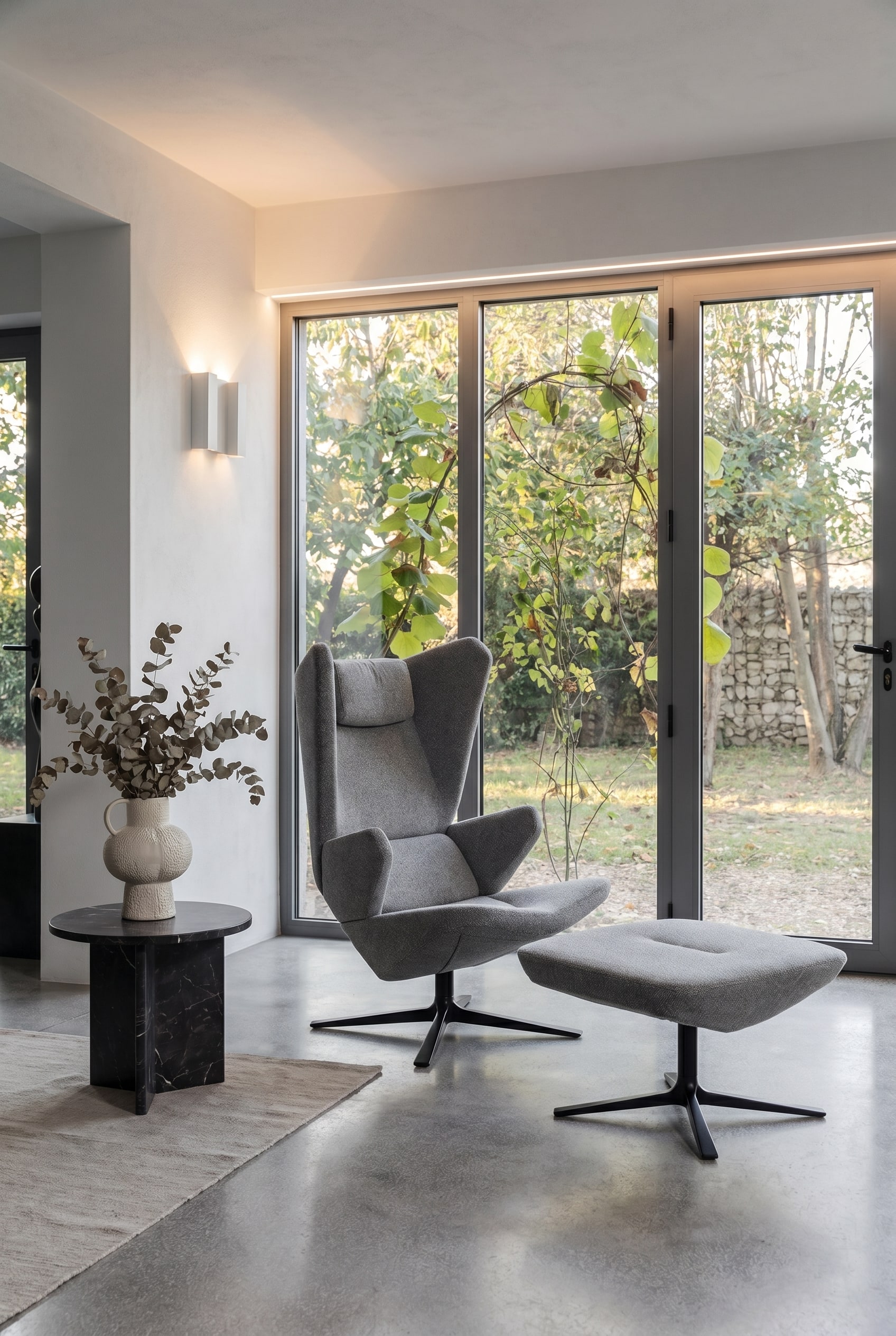 Modern living room with Trifidae armchair in grey textured fabric, side table with ceramic vase, and large windows
