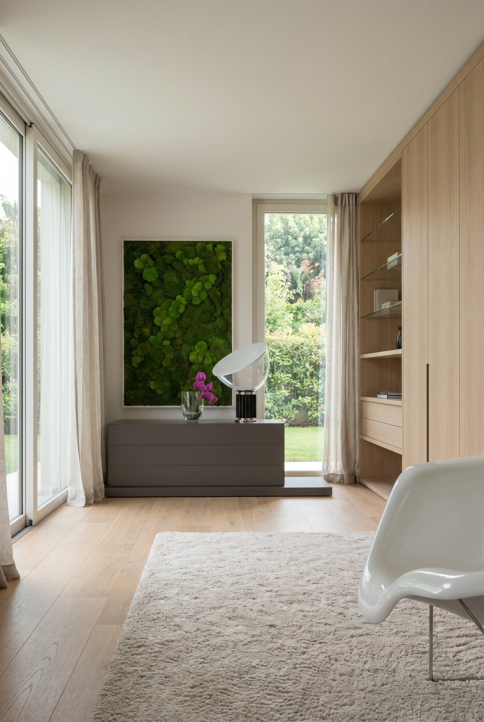 Elegantes Schlafzimmer mit niedriger, dunkelgrauer Kommode, dar&uuml;ber ein Moosbild und ein wei&szlig;er Schalenstuhl