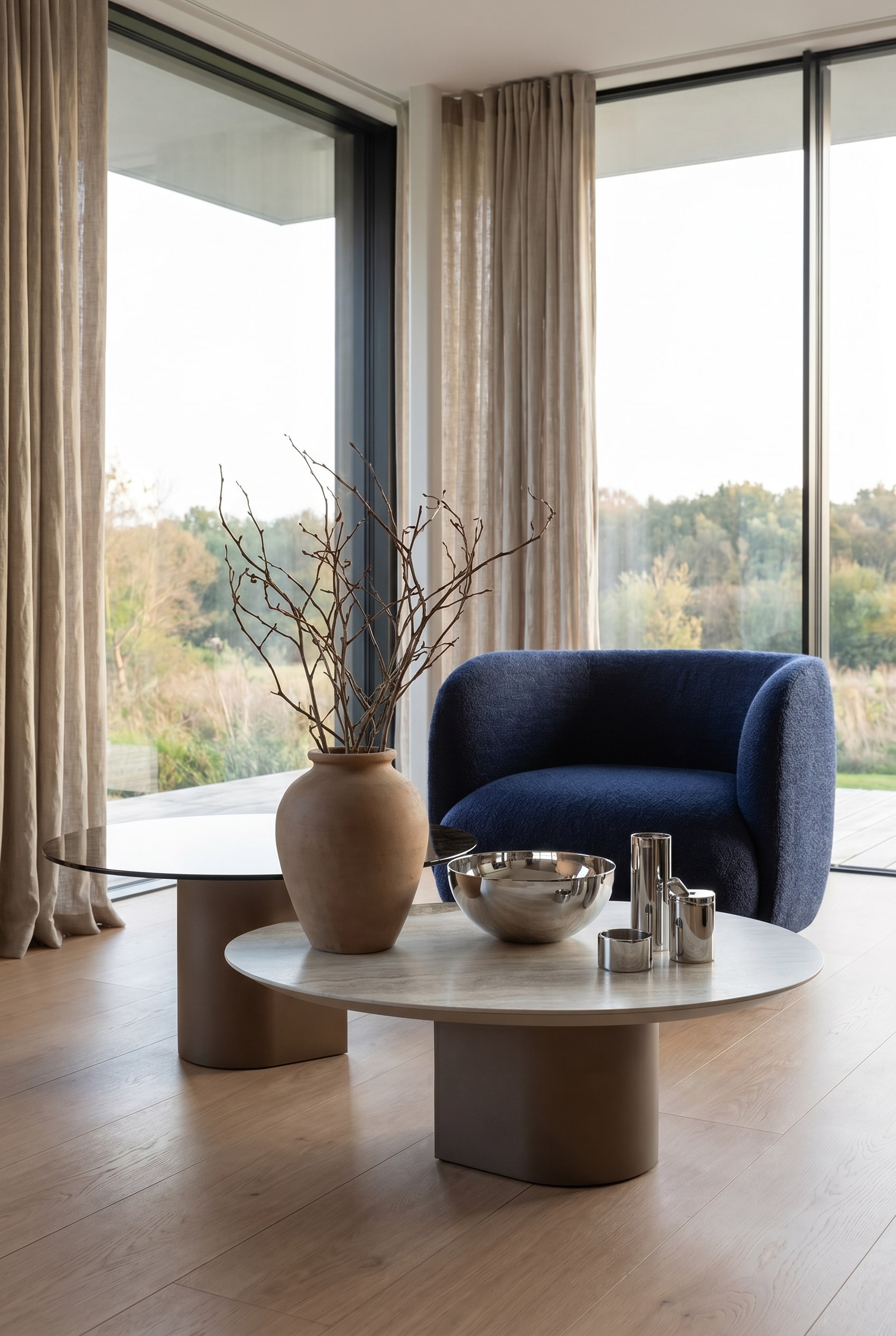 Wohnzimmer mit skulpturalem Couchtisch, dekoriert mit einer matten Tonvase, trockenen Zweigen und einer polierten Edelstahl-Schale