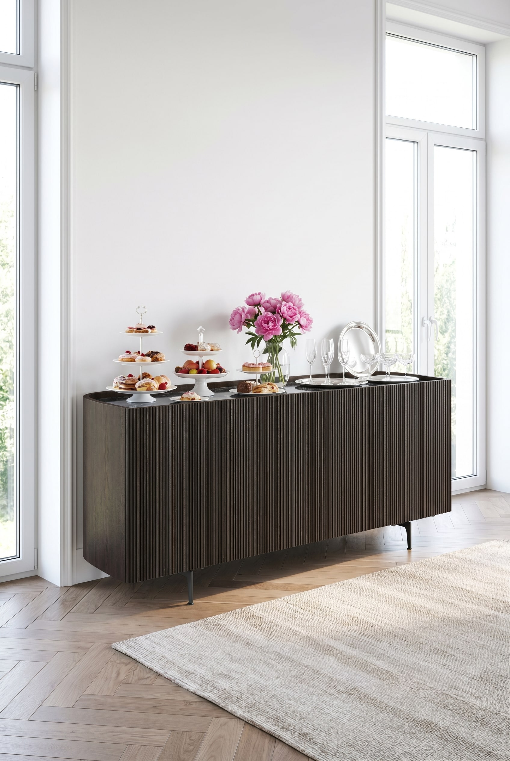 Dunkles Novamobili Bay Sideboard mit abgerundeten Ecken und geriffelter Front in einem hellen Raum, dekoriert mit weißen Porzellantellern und rosa Pfingstrosen. Dunkles Novamobili Bay Sideboard mit abgerundeten Ecken und geriffelter Front in einem hellen Raum, dekoriert mit weißen Porzellantellern und rosa Pfingstrosen.