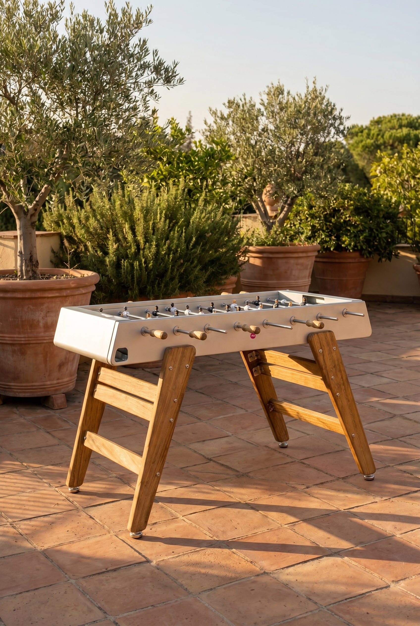 Mediterranean terrace with Iroko wood foosball table and large planters in warm evening light