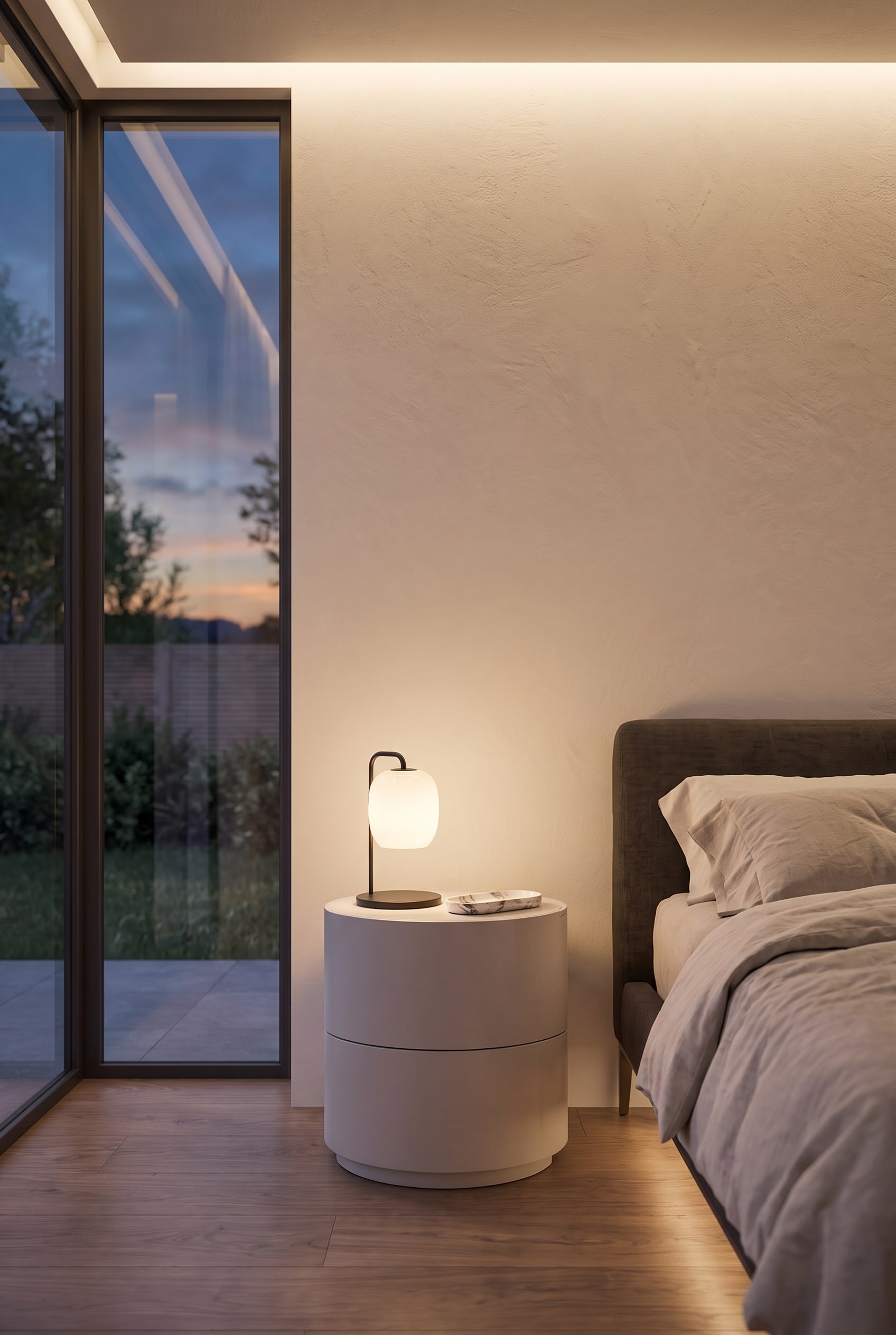 Cylindrical, matte bedside table with two drawers directly next to a modern upholstered bed.