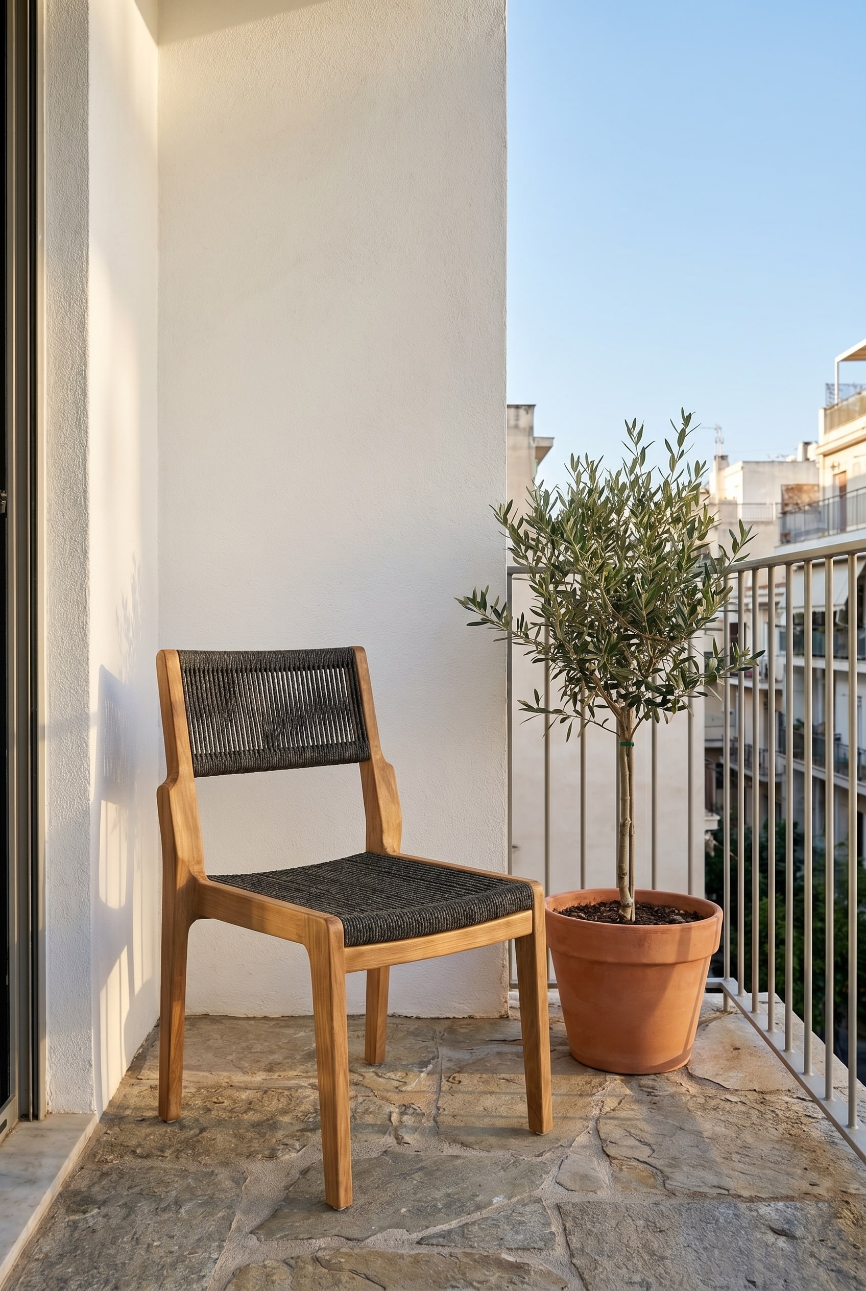 Kompakter Balkon mit Natursteinboden und einem Teakholz-Stuhl mit anthrazitfarbenem Seilgeflecht im sanften Morgenlicht