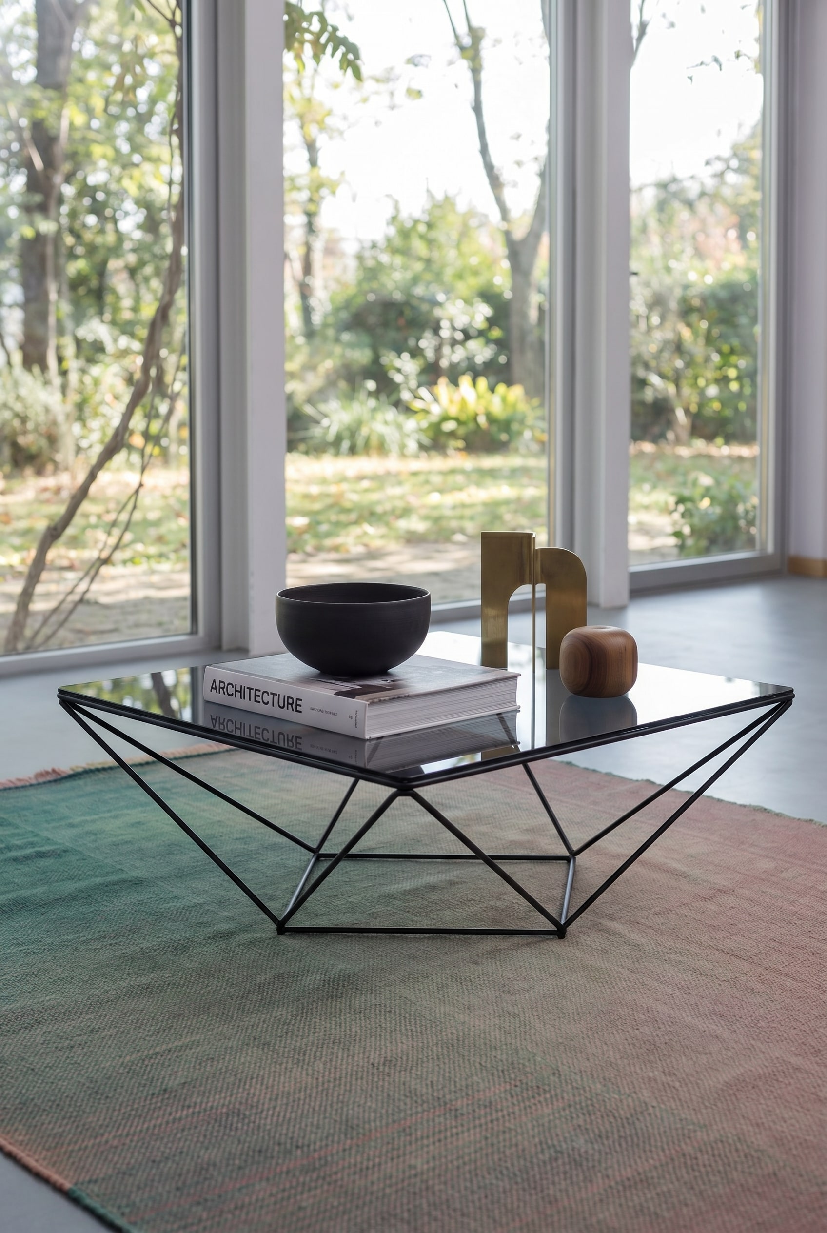 Luftiges Wohnzimmer mit quadratischem Glas-Couchtisch mit feinem Metallrahmen, darauf ein Architektur-Bildband und eine dunkle Keramikschale