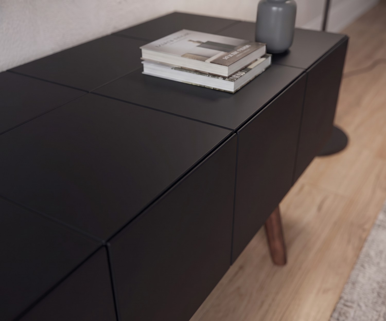 al2 TV Lowboard MOS-I-KO 005 B in Mattschwarz im Wohnzimmer, Detailaufnahme der grifflosen Front und Holzbeine im Retro-Stil.