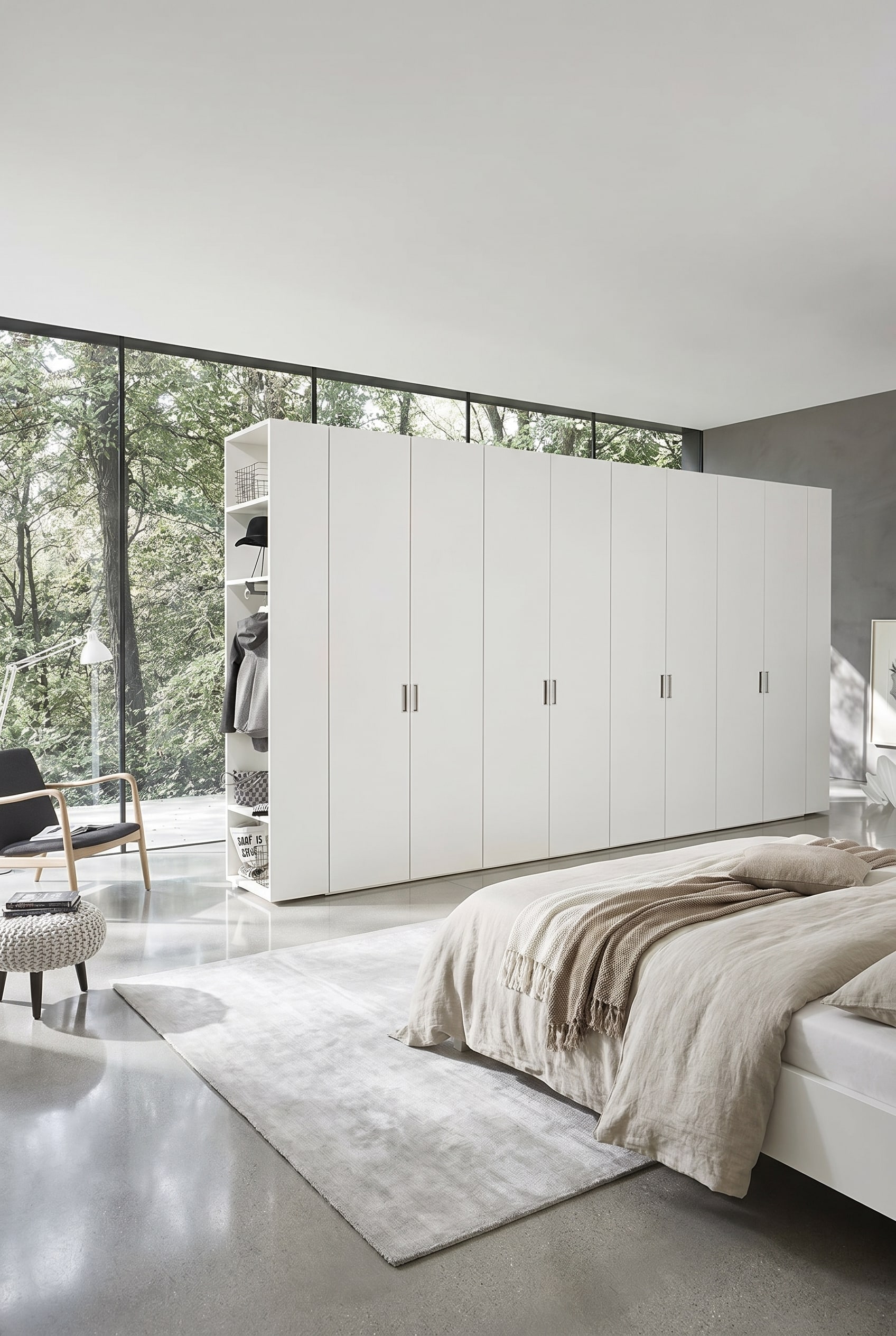 Wide, white wardrobe wall with minimalist hinged doors and delicate metal handles, concluded on the left side by an open shelf module