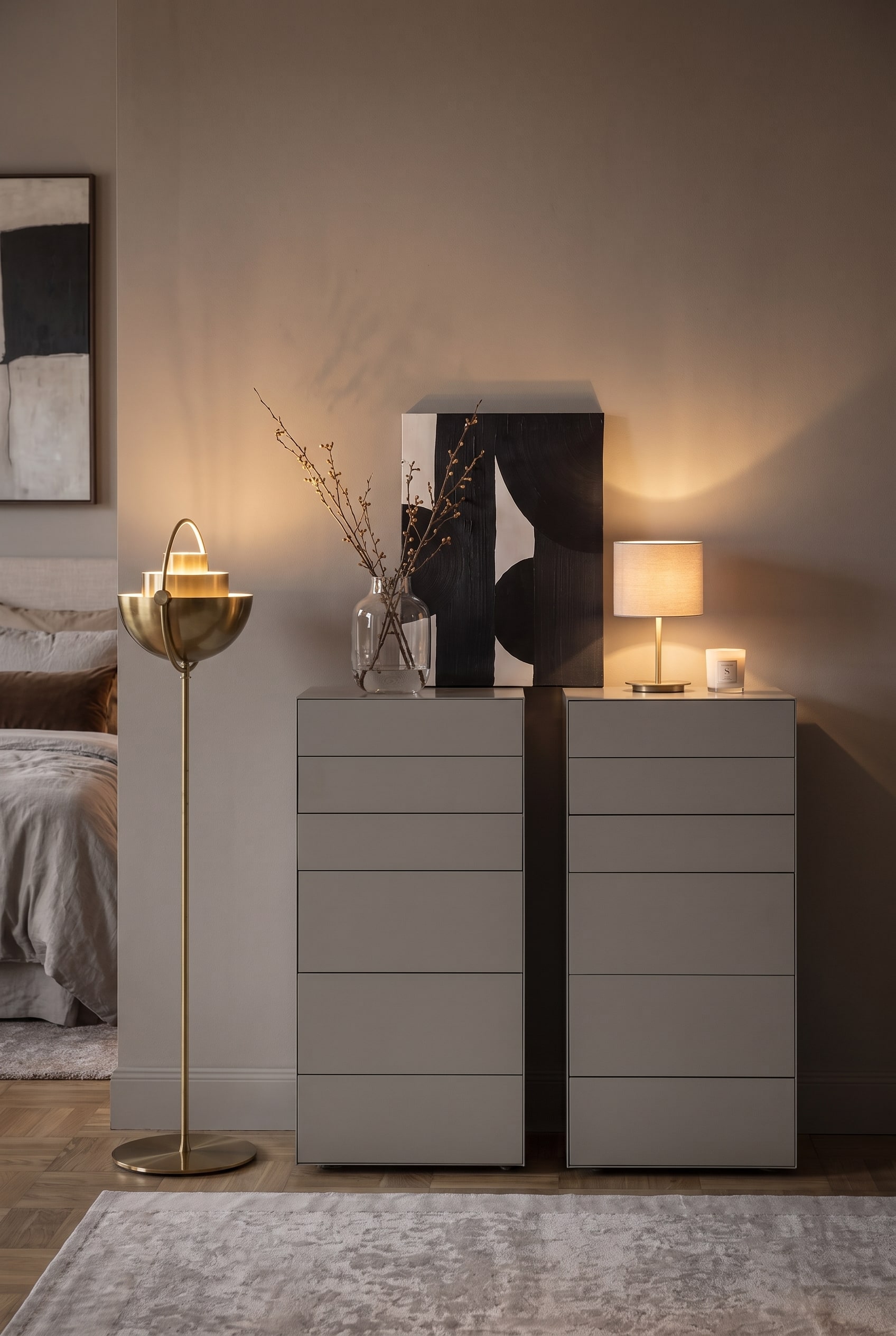 Frontal view of two grey tall chests of drawers with asymmetrical decoration and a golden floor lamp on the left.