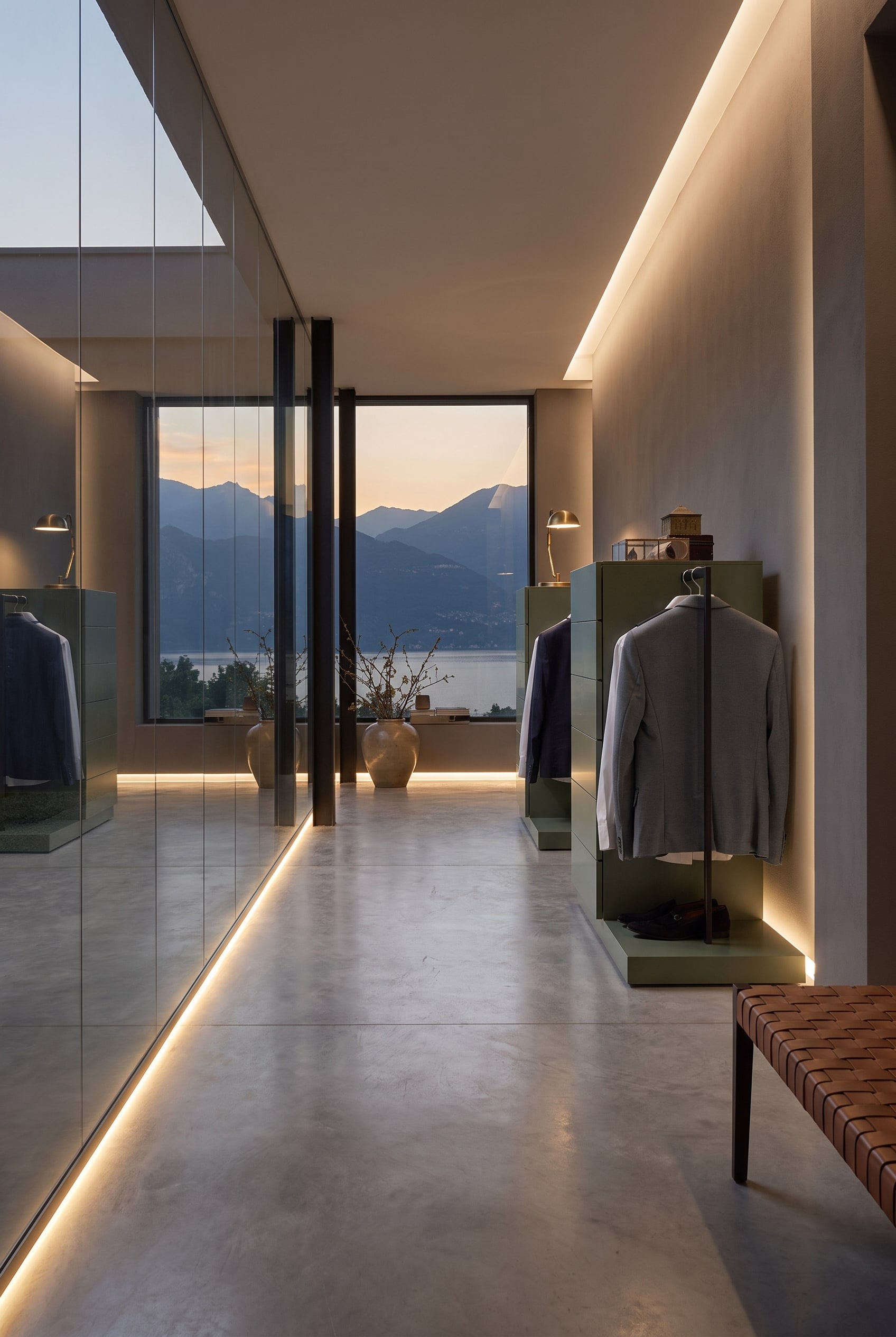 Two olive green chests of drawers with concealed clothes rails in a modern hallway with a mirror wall and mountain view through the window.