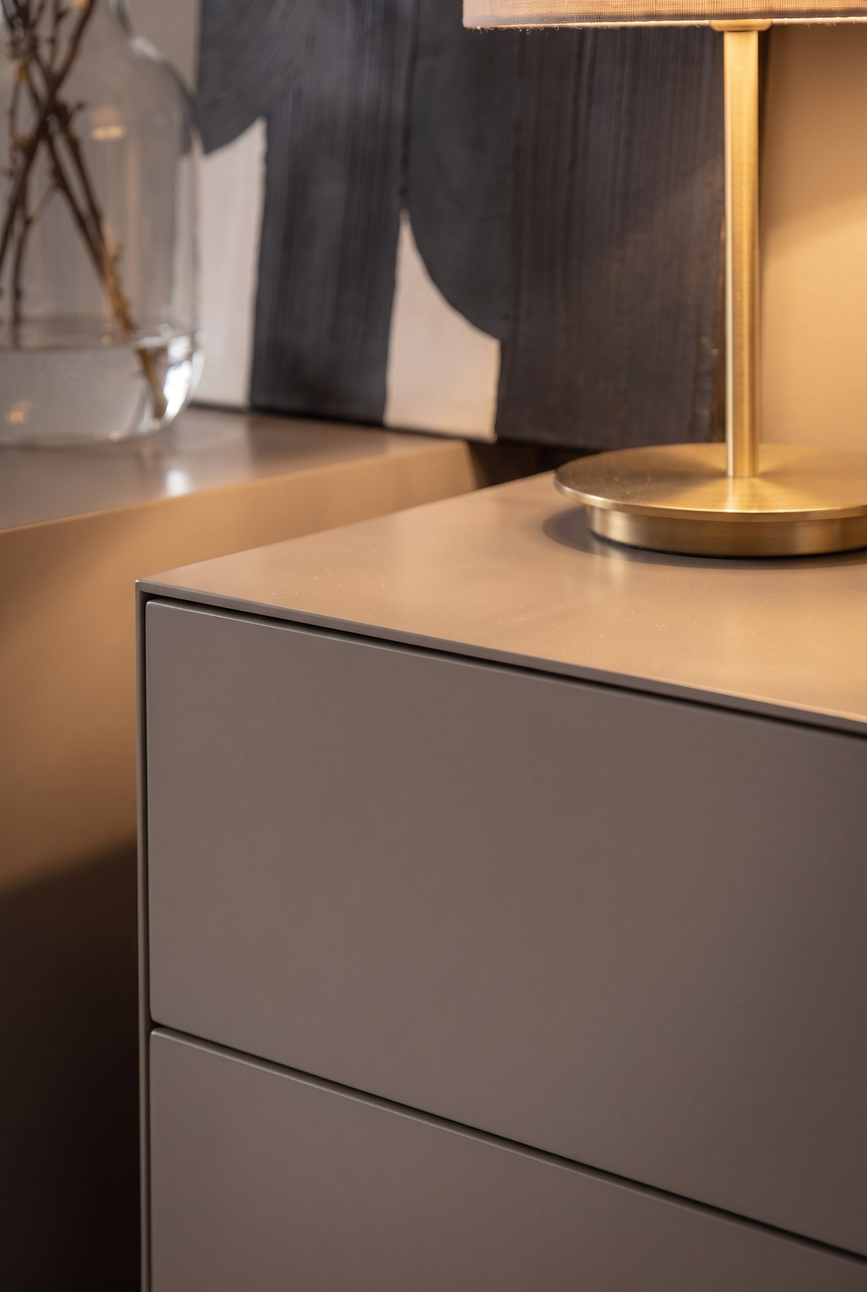 Close-up of the edge of a matte gray designer chest of drawers with a brass-colored lamp base.