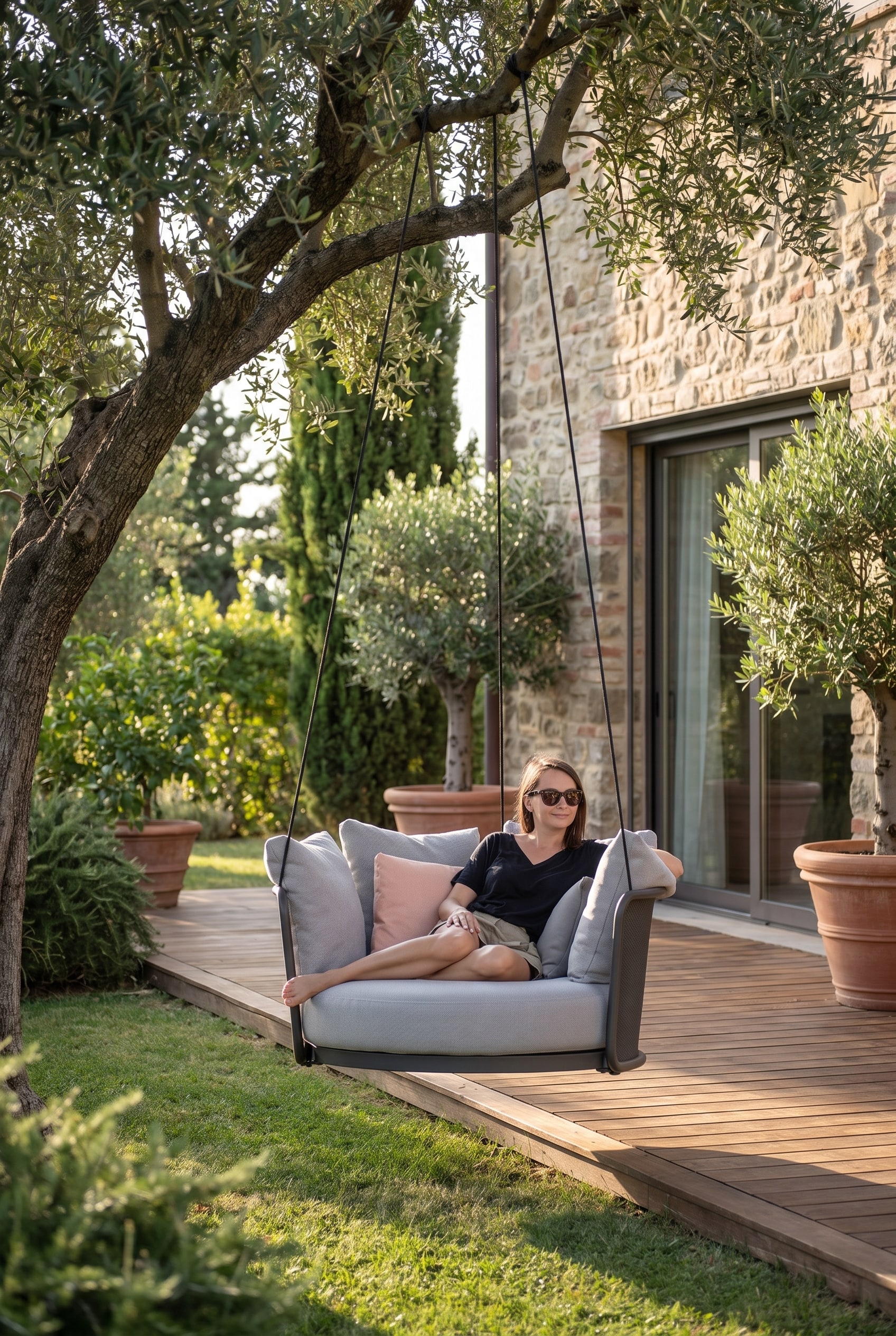 Green terrace edge with a floating, grey hanging chair, attached to a modern frame in the cool partial shade of a tree