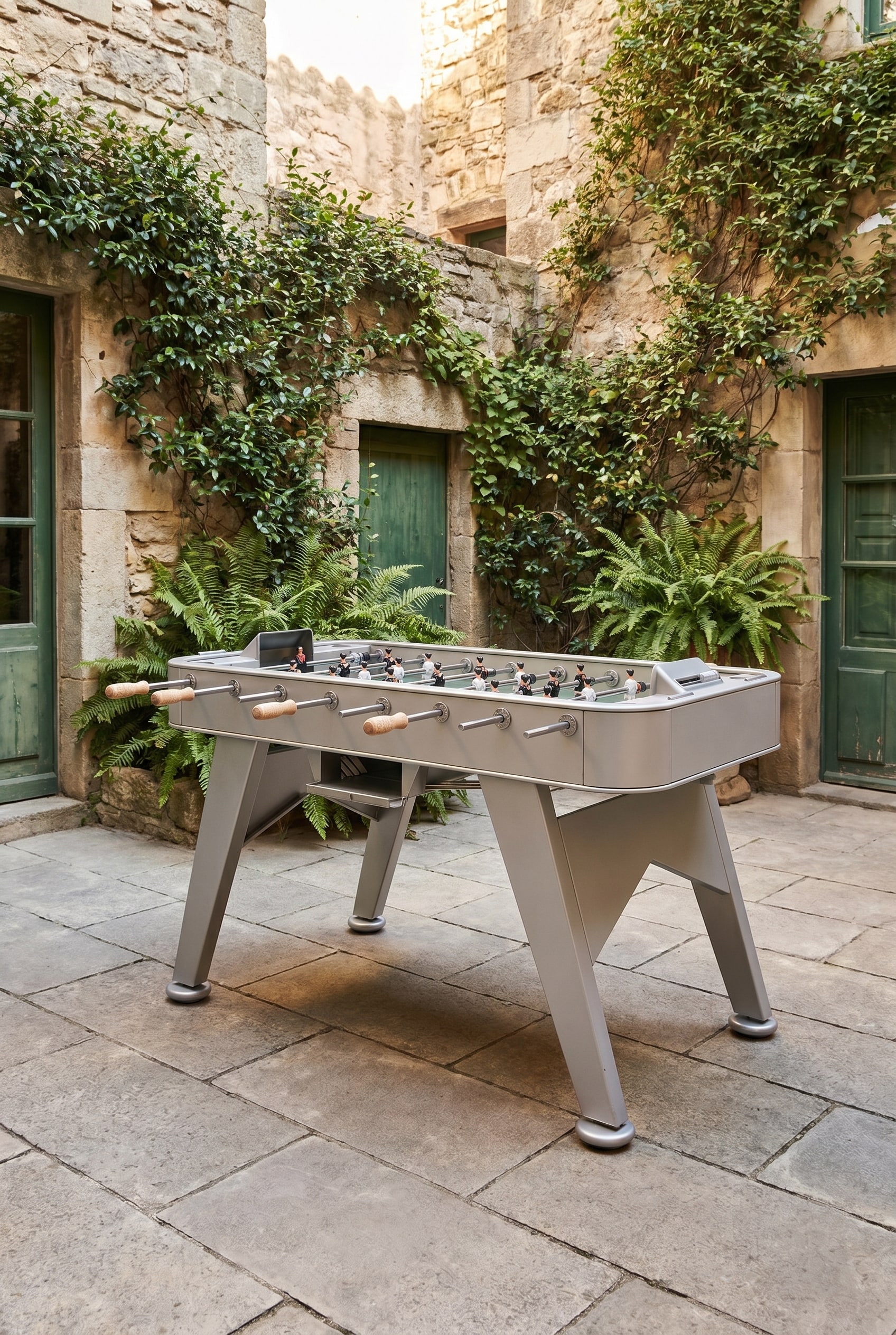 Urban courtyard with stone floor tiles and a silver steel foosball table next to a planted stone wall