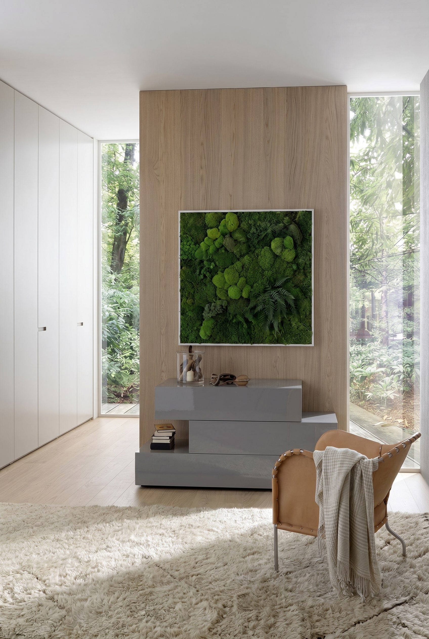 Modernes Schlafzimmer mit grauer, asymmetrischer Kommode in Hochglanz, dar&uuml;ber ein gerahmtes Moosbild und ein lederner Sessel